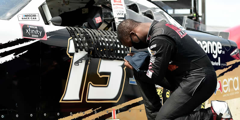 Jesse Iwuji kneels in prayer next to his car